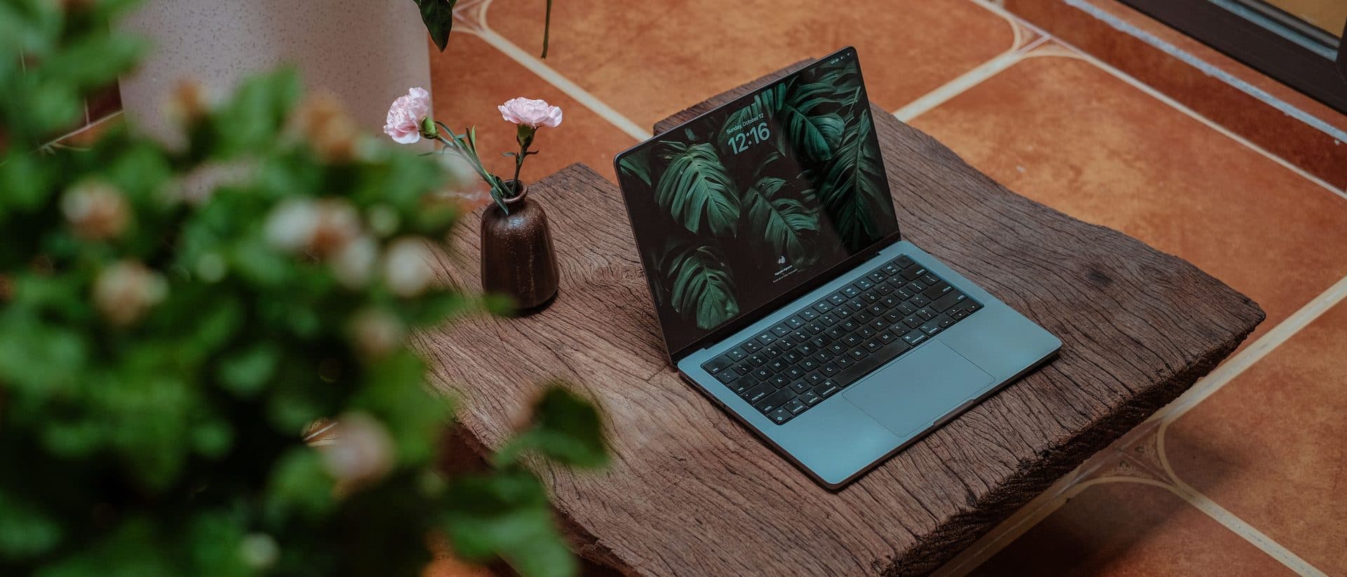 A MacBook on a rustic wooden table beside fresh flowers