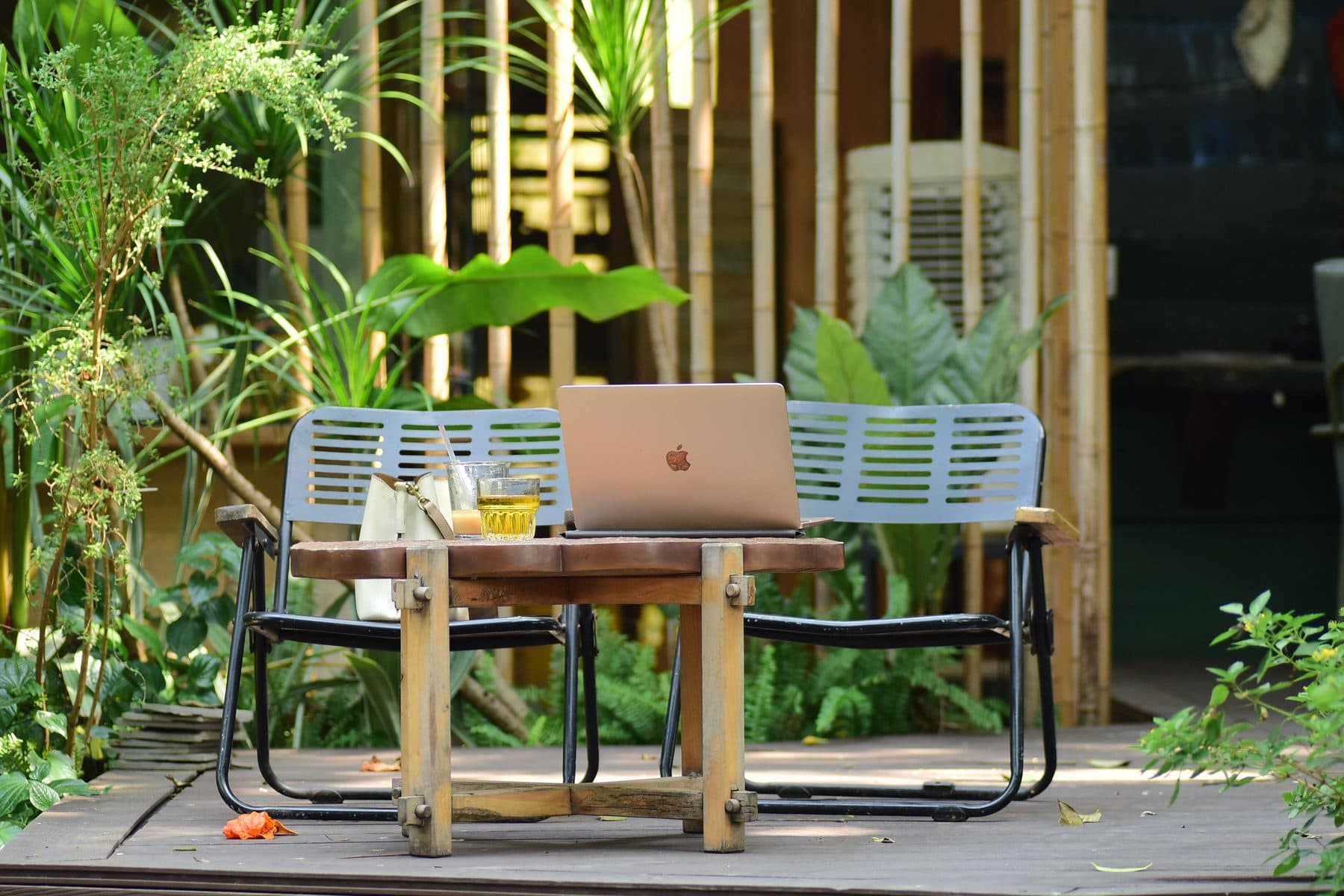 A laptop set up on a wooden table in a green garden courtyard