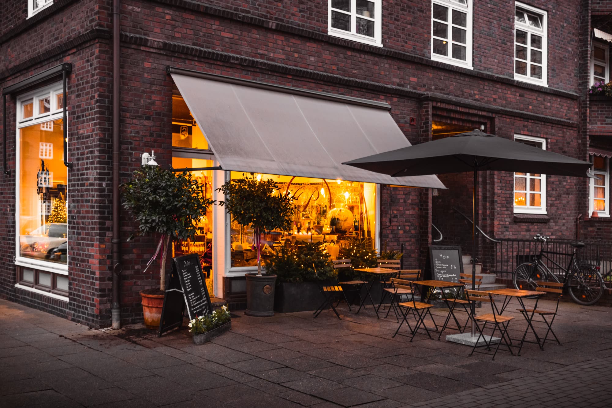 A warmly lit corner café with outdoor tables at dusk